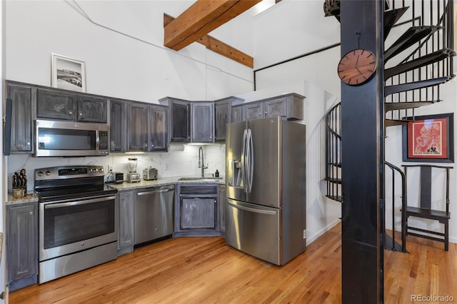 kitchen featuring sink, light stone counters, tasteful backsplash, stainless steel appliances, and light hardwood / wood-style floors