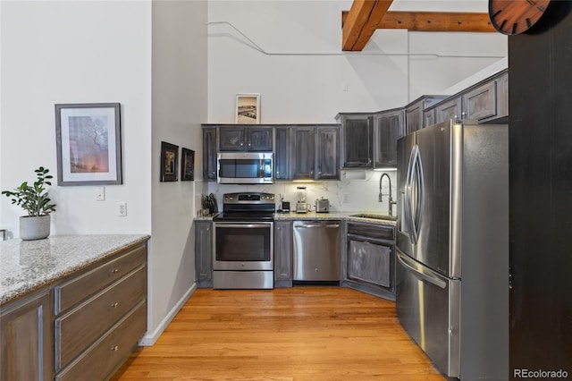 kitchen featuring dark brown cabinetry, appliances with stainless steel finishes, sink, and light stone counters