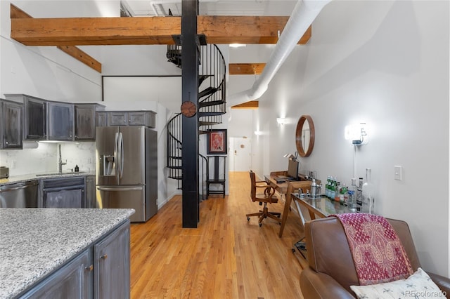 kitchen featuring sink, stainless steel appliances, beam ceiling, light hardwood / wood-style floors, and backsplash