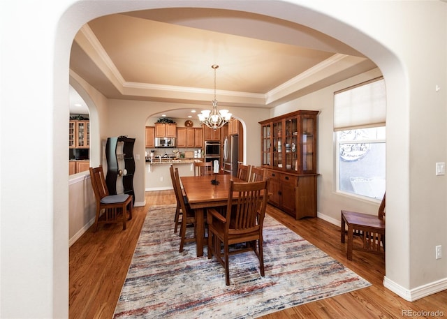 5279 Mount Cutler Ct, Colorado Springs, CO 80924 - dining space with arched walkways, a chandelier, light wood-type flooring, a tray ceiling, and ornamental molding