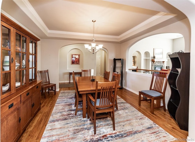 5279 Mount Cutler Ct, Colorado Springs, CO 80924 - dining room featuring arched walkways, a chandelier, a raised ceiling, and light wood-style floors
