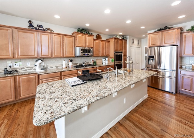 5279 Mount Cutler Ct, Colorado Springs, CO 80924 - kitchen featuring decorative backsplash, a center island with sink, light stone counters, light wood-style floors, and stainless steel appliances