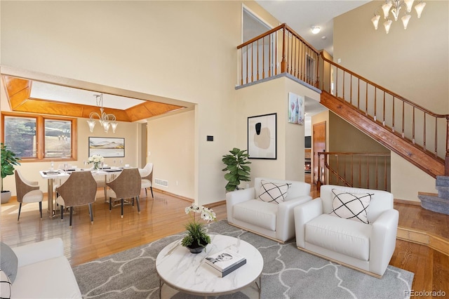 living area with visible vents, an inviting chandelier, wood finished floors, and stairs