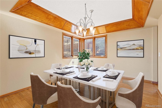 dining area with a tray ceiling, a notable chandelier, baseboards, and light wood finished floors