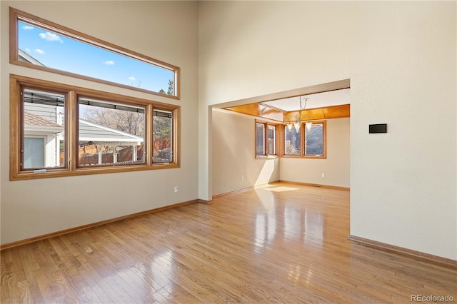 empty room with baseboards, wood-type flooring, a high ceiling, and a chandelier