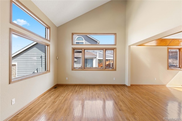 spare room featuring light wood-style floors, baseboards, and high vaulted ceiling