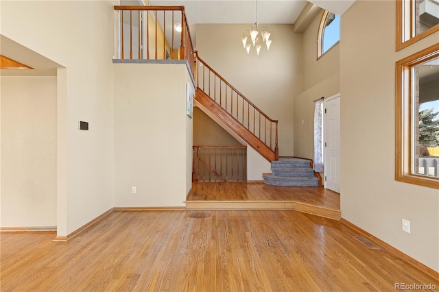 unfurnished living room with visible vents, wood finished floors, stairs, and a chandelier