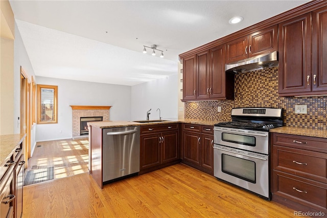 kitchen featuring under cabinet range hood, a sink, backsplash, light wood-style floors, and appliances with stainless steel finishes