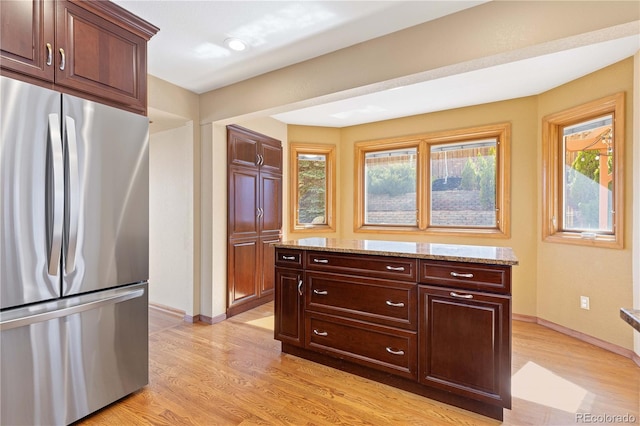 kitchen featuring light wood finished floors, baseboards, freestanding refrigerator, and light stone counters