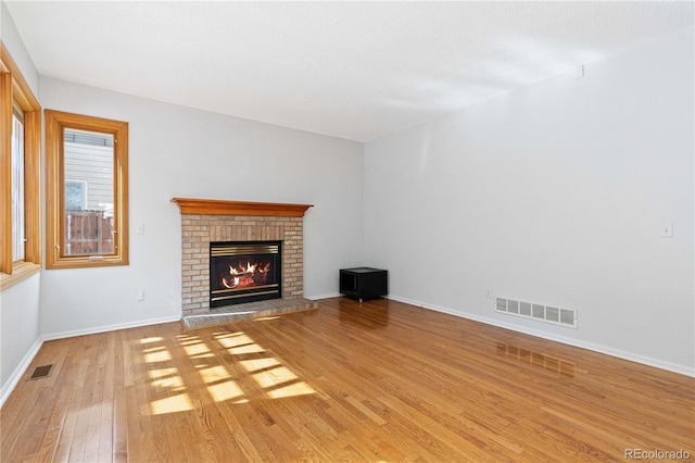 unfurnished living room featuring a brick fireplace, light wood-style flooring, baseboards, and visible vents