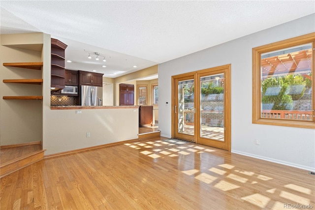 unfurnished living room featuring a wealth of natural light, light wood-style flooring, a textured ceiling, and baseboards