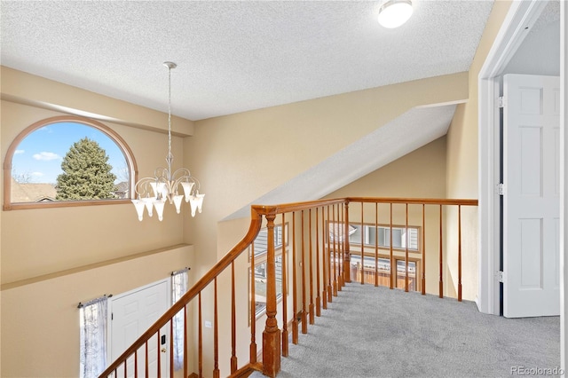 corridor with a textured ceiling, lofted ceiling, carpet floors, and a chandelier