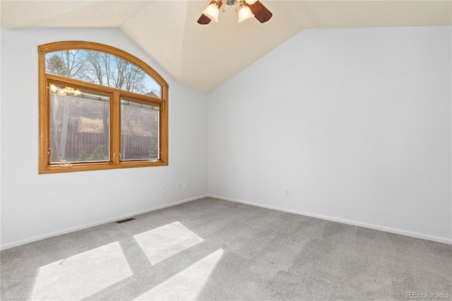 carpeted empty room featuring lofted ceiling, baseboards, visible vents, and ceiling fan