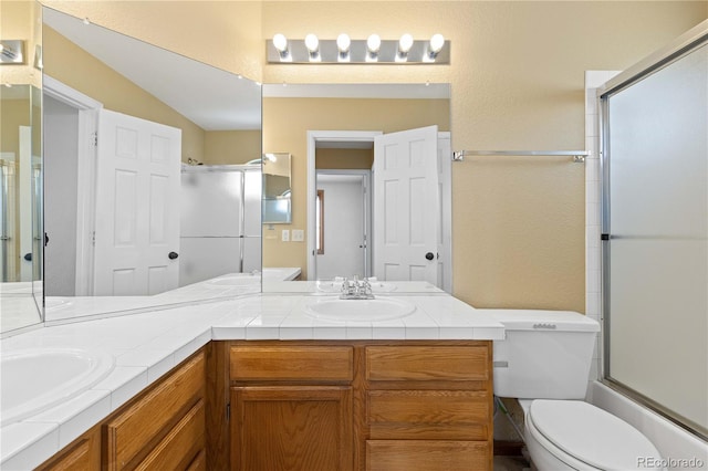 bathroom featuring a shower with door, toilet, double vanity, and a sink