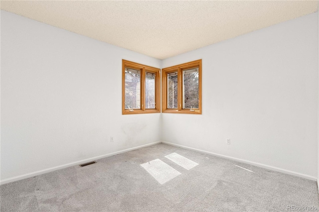 carpeted spare room featuring baseboards, visible vents, and a textured ceiling