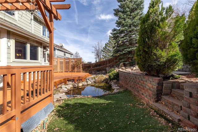 view of yard featuring a garden pond, a deck, and fence