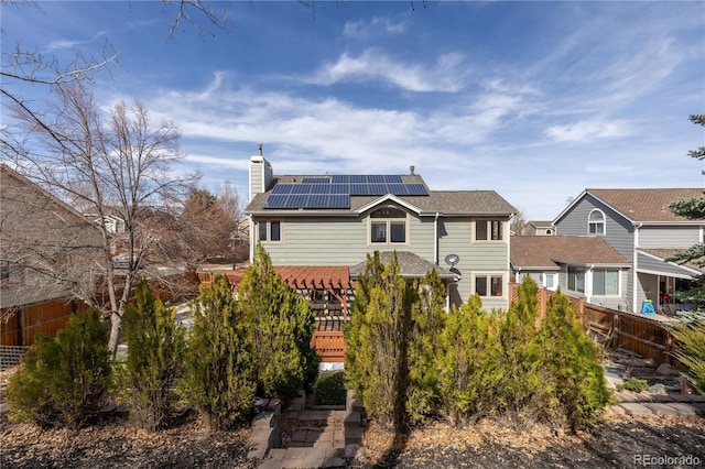 view of front of house featuring a deck, roof mounted solar panels, fence, a shingled roof, and a chimney