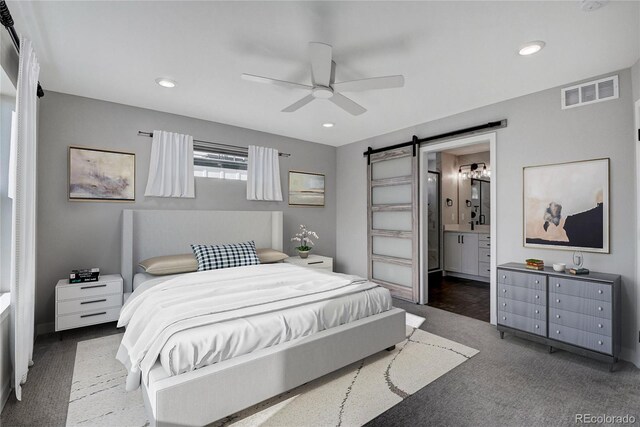 carpeted bedroom with a barn door, ensuite bathroom, and ceiling fan