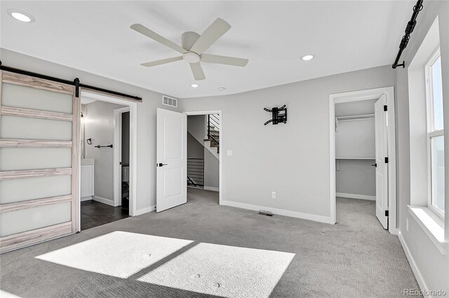 unfurnished bedroom featuring carpet flooring, multiple windows, ceiling fan, and a barn door