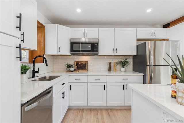 kitchen featuring sink, backsplash, stainless steel appliances, white cabinets, and light wood-type flooring