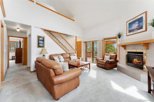 carpeted living area with a tile fireplace, high vaulted ceiling, baseboards, and stairs