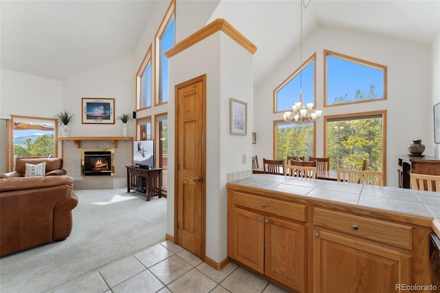kitchen featuring tile countertops, high vaulted ceiling, an inviting chandelier, light carpet, and a tile fireplace