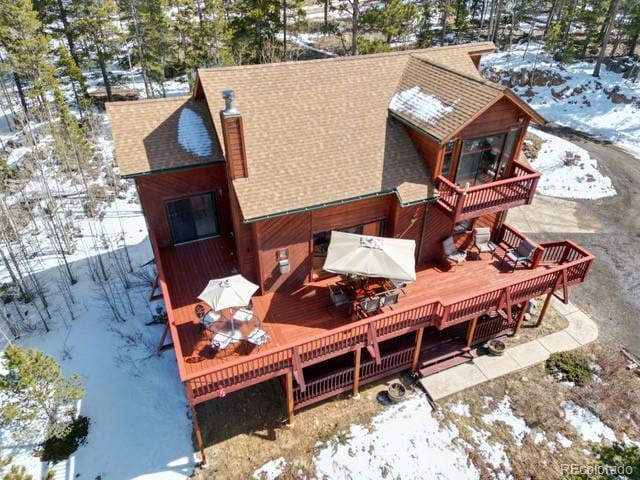 snow covered back of property with a wooden deck and roof with shingles