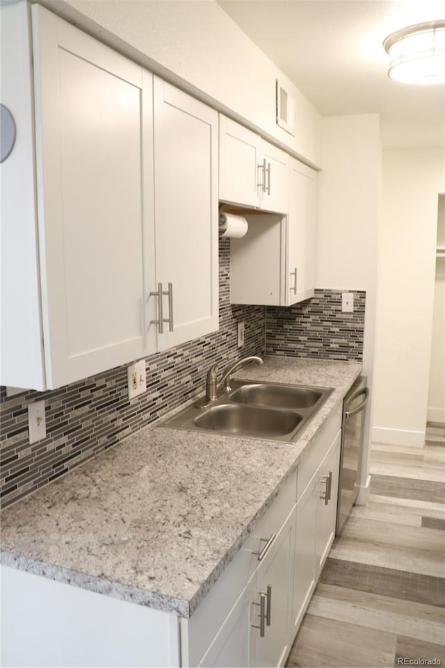 kitchen featuring white cabinetry, sink, stainless steel dishwasher, backsplash, and light wood-type flooring