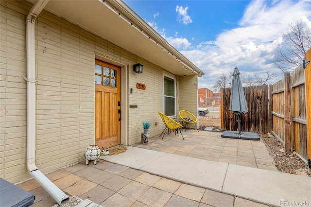 view of exterior entry featuring a patio area, fence, and brick siding