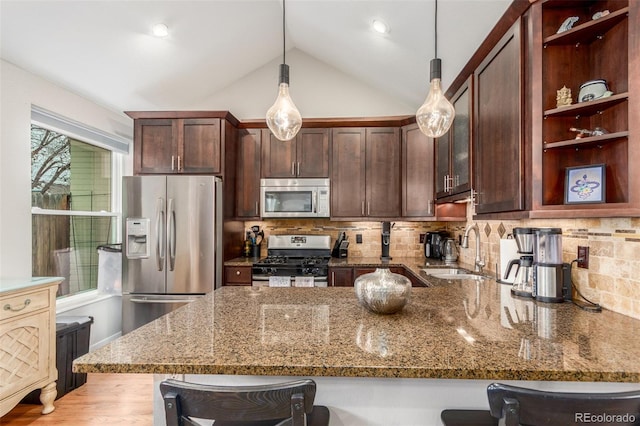 kitchen featuring stone countertops, stainless steel appliances, a sink, a kitchen breakfast bar, and hanging light fixtures