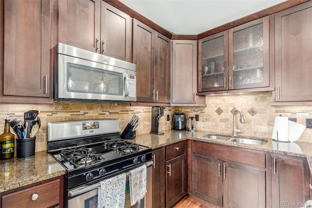 kitchen featuring light stone counters, stainless steel appliances, a sink, tasteful backsplash, and glass insert cabinets