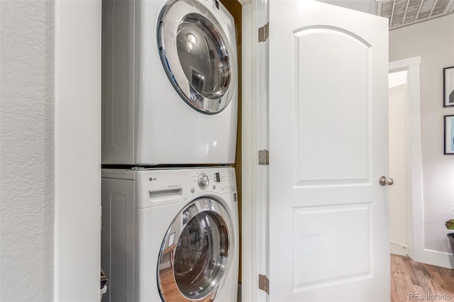 washroom featuring a textured wall, laundry area, wood finished floors, visible vents, and stacked washer and clothes dryer