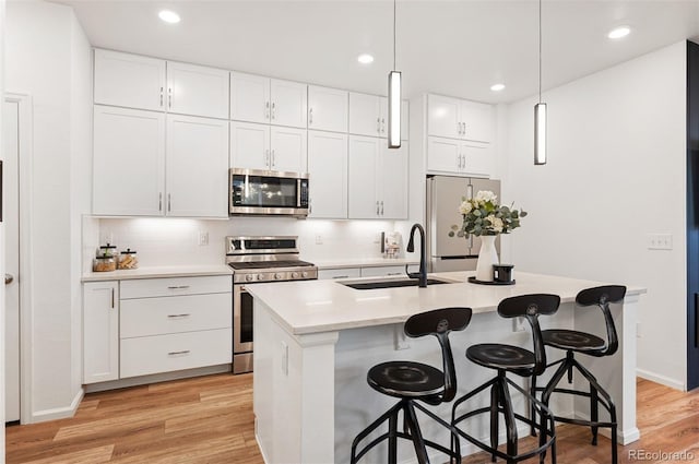 kitchen with light countertops, appliances with stainless steel finishes, a kitchen island with sink, white cabinets, and a sink