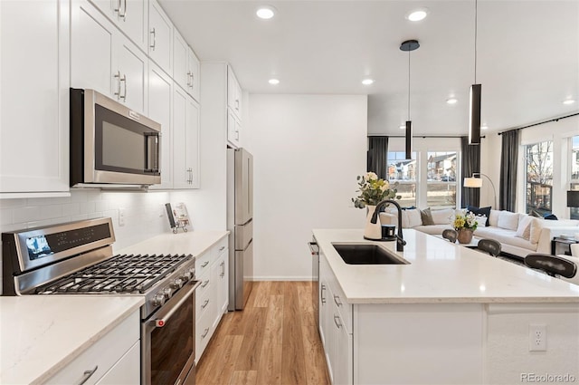 kitchen featuring stainless steel appliances, an island with sink, a sink, and pendant lighting