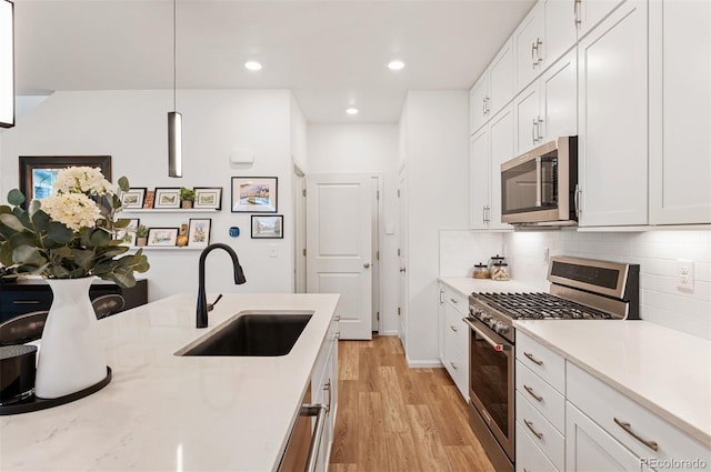 kitchen featuring appliances with stainless steel finishes, decorative light fixtures, a sink, and white cabinetry