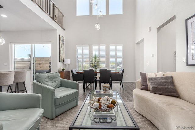 living room featuring a towering ceiling, baseboards, plenty of natural light, and wood finished floors