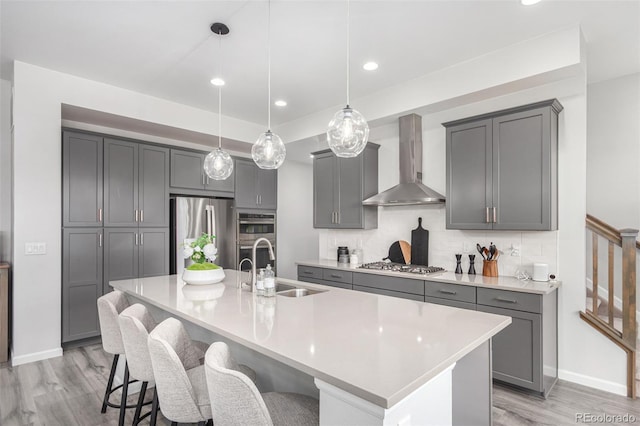 kitchen with a sink, gray cabinets, wall chimney exhaust hood, light wood-style flooring, and appliances with stainless steel finishes