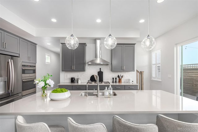 kitchen featuring a sink, wall chimney range hood, a kitchen breakfast bar, and appliances with stainless steel finishes