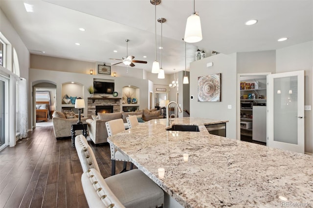 335 Mountain Brush, Colorado Springs, CO 80921 - kitchen with a sink, a ceiling fan, dark wood-style floors, light stone countertops, and a stone fireplace