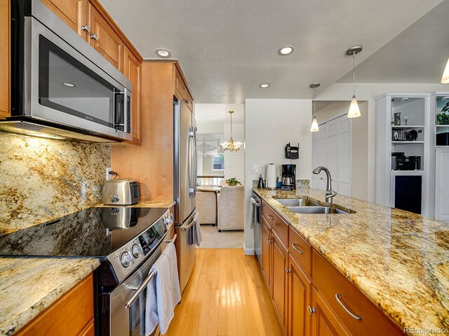 1011 N Pennsylvania St Unit H, Denver, CO 80203 - kitchen featuring a sink, appliances with stainless steel finishes, brown cabinetry, light stone countertops, and light wood finished floors
