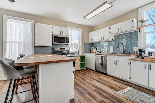 kitchen featuring wooden counters, white cabinetry, a sink, light wood finished floors, and appliances with stainless steel finishes