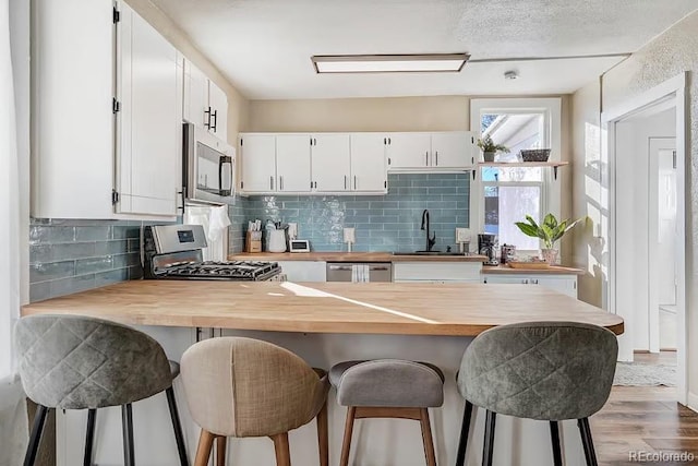 kitchen with a sink, stainless steel appliances, a peninsula, wood finished floors, and butcher block counters