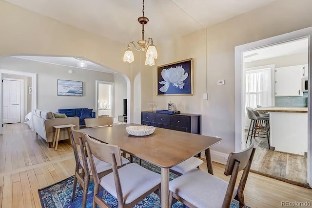 dining space with arched walkways, light wood finished floors, and a chandelier