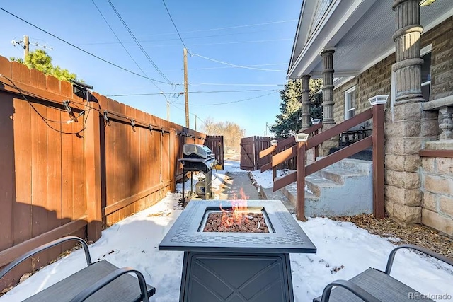 snow covered patio with fence, a fire pit, and area for grilling