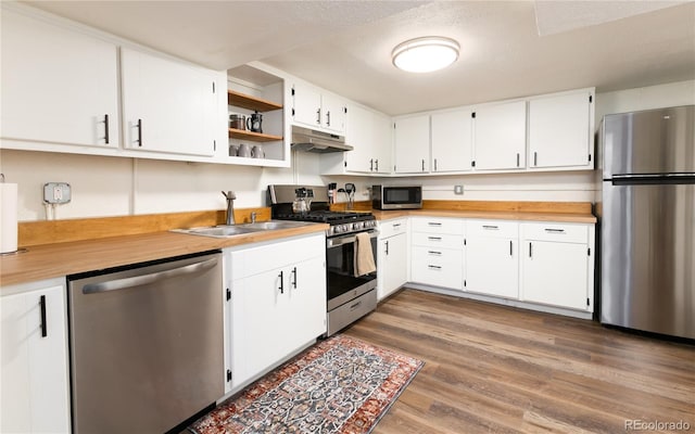 kitchen with appliances with stainless steel finishes, wood finished floors, a sink, under cabinet range hood, and white cabinetry