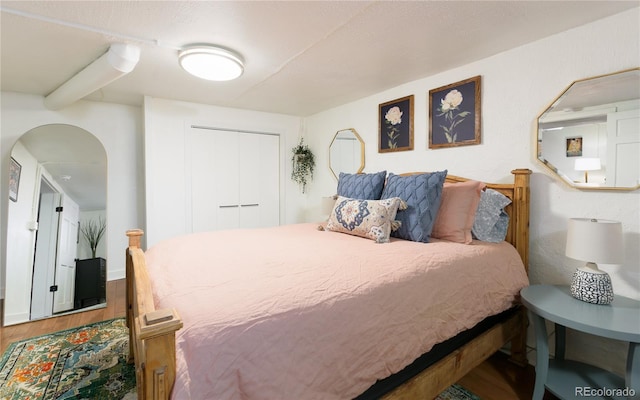 bedroom with arched walkways, wood finished floors, and a closet