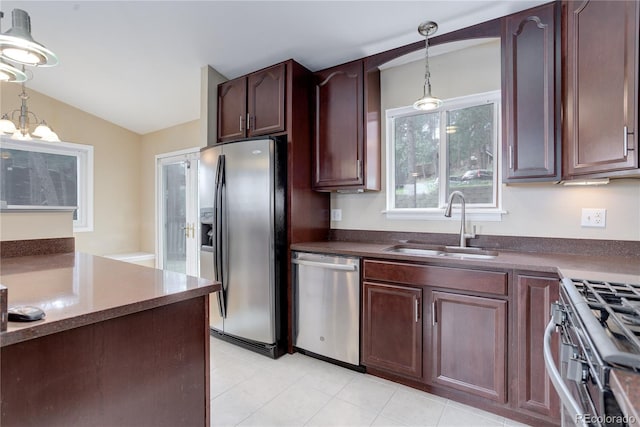 kitchen with dark countertops, hanging light fixtures, appliances with stainless steel finishes, a sink, and vaulted ceiling