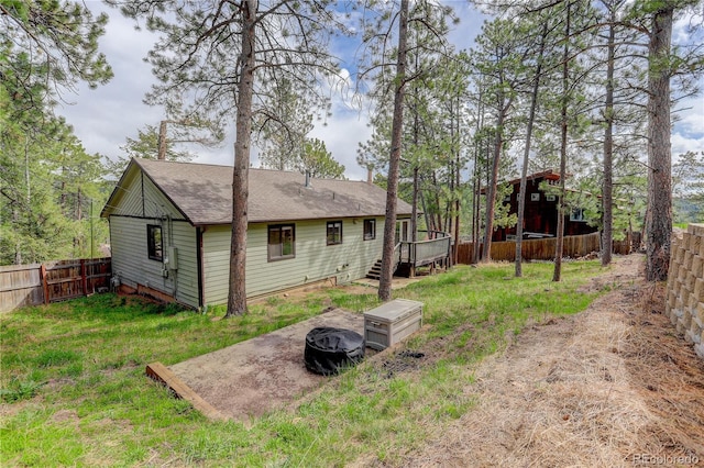 back of house featuring a shingled roof, a deck, a fenced backyard, a yard, and a fire pit