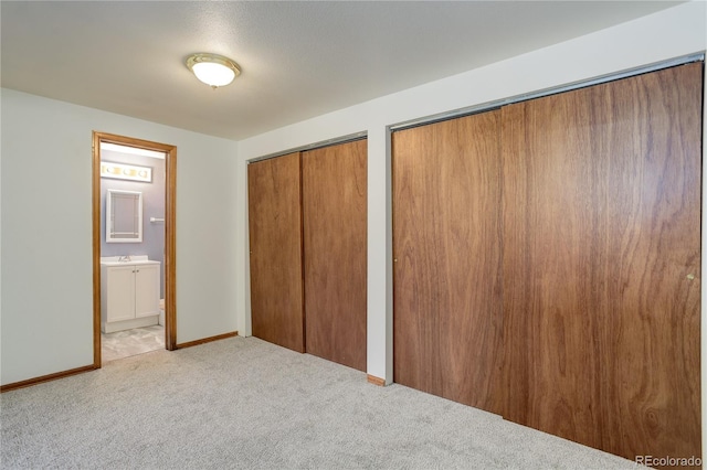unfurnished bedroom with connected bathroom, baseboards, multiple closets, and carpet
