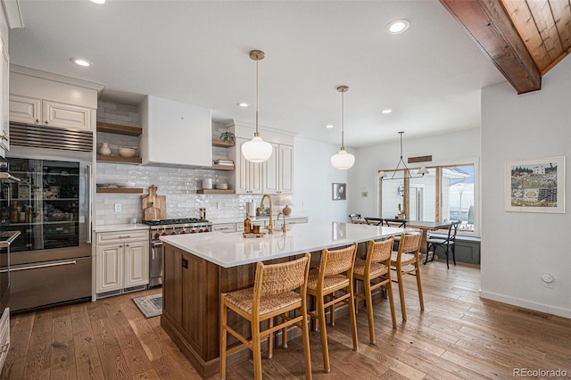 kitchen with a breakfast bar, sink, hanging light fixtures, high end appliances, and a kitchen island with sink